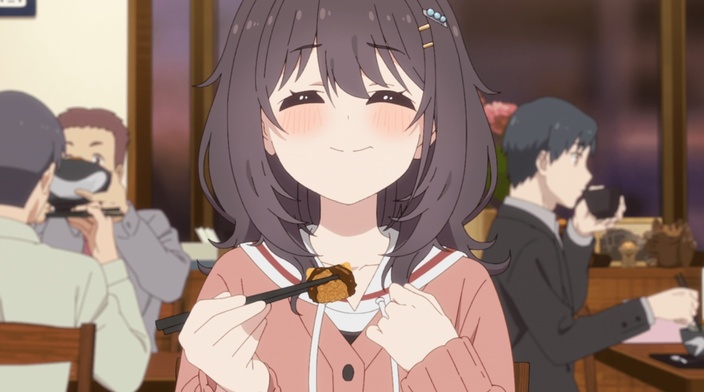 Mako holding a piece of tonkatsu with chopsticks and a delighted expression